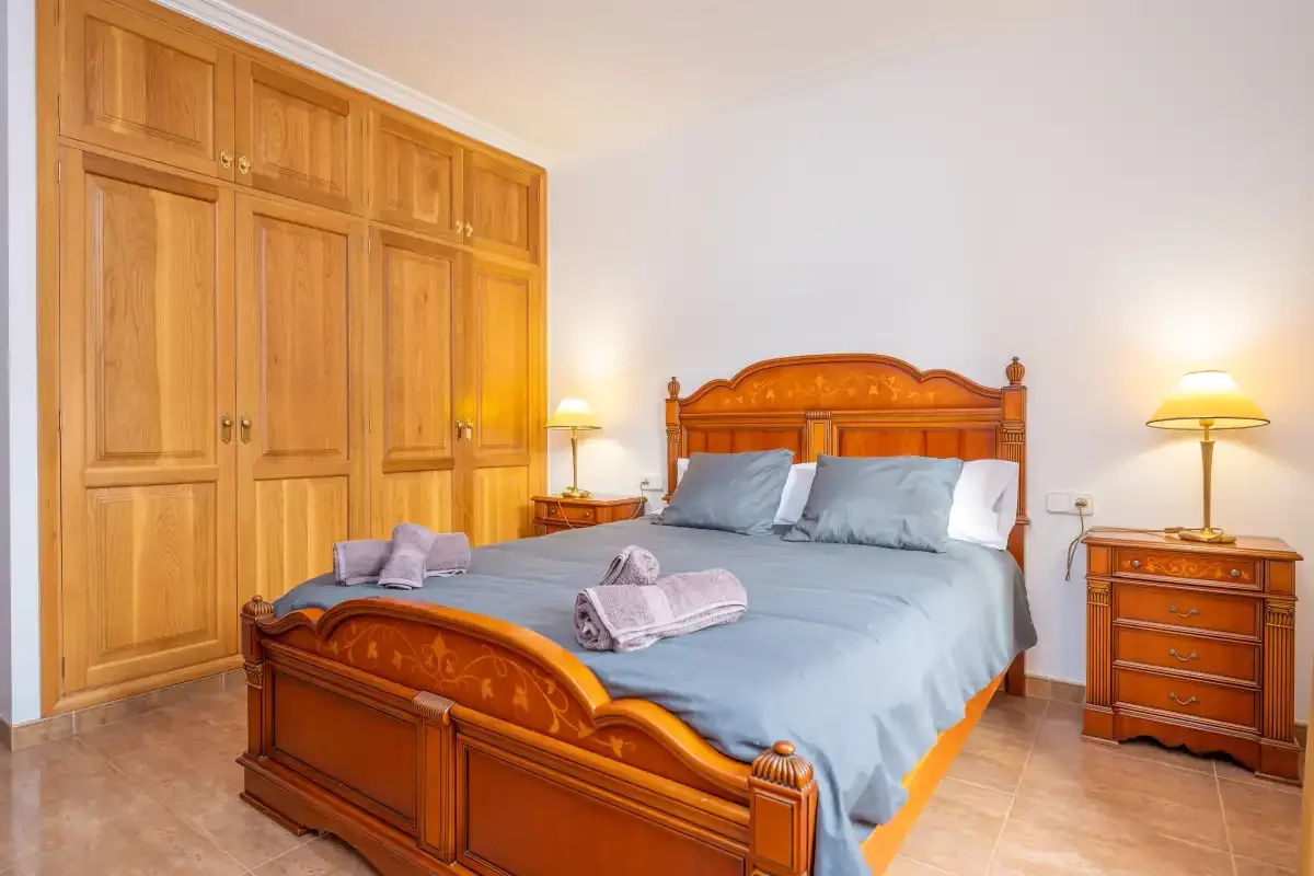 Un dormitorio con cama de madera, ropa de cama azul y armarios a juego.