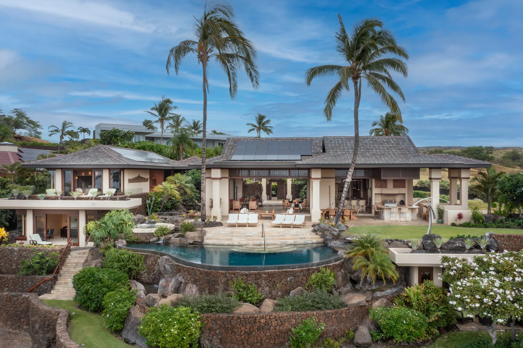Un edificio de estilo tropical da a una piscina curva, rodeada de jardines y palmeras.
