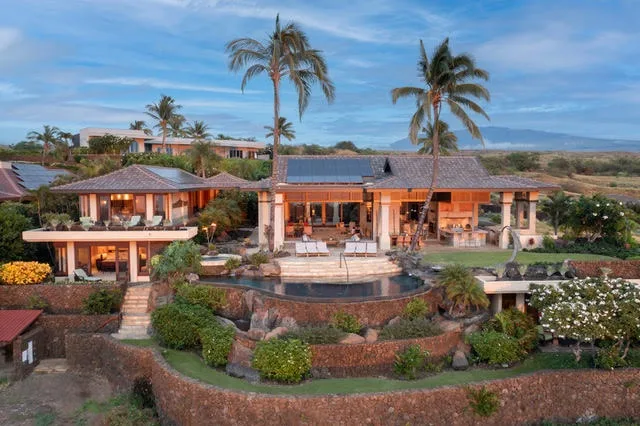 Una amplia residencia tropical con una piscina curva, jardines y palmeras.