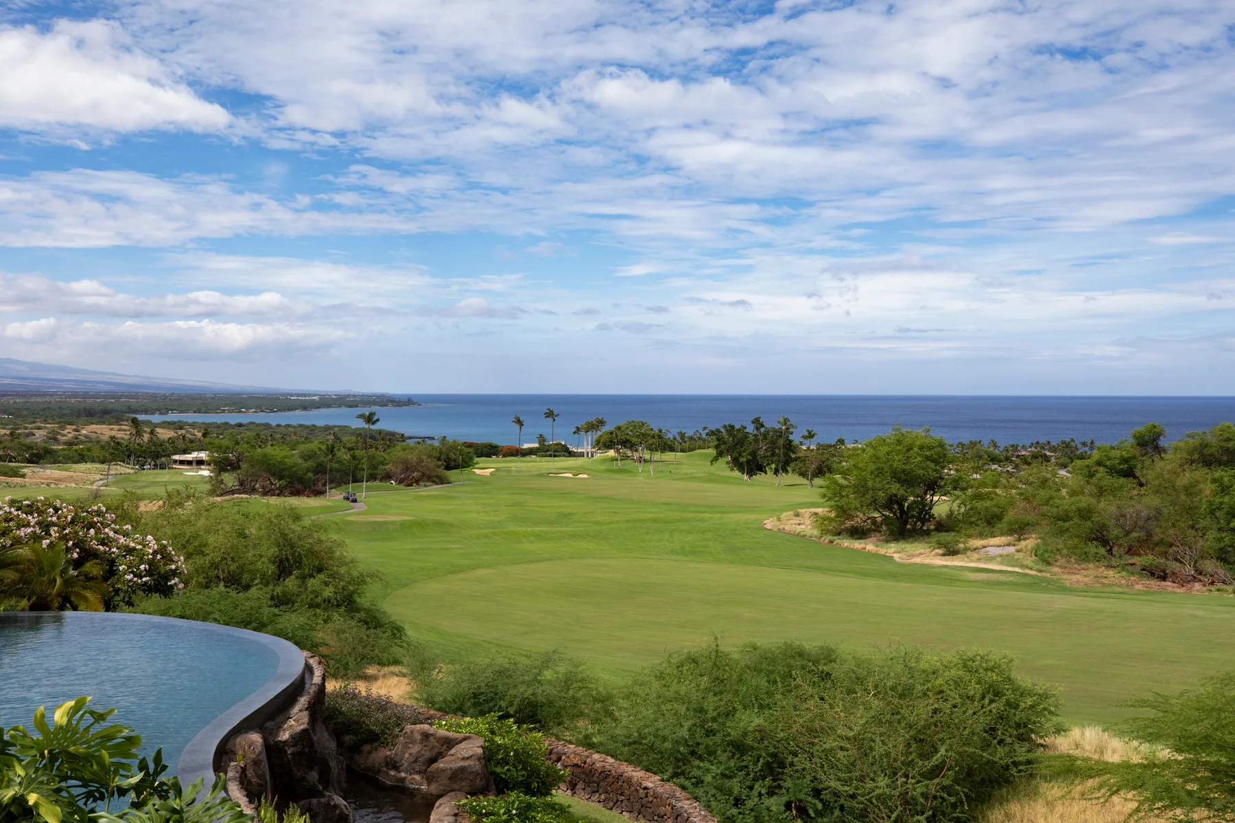 Un campo de golf ajardinado se extiende hacia el océano bajo un cielo parcialmente nublado.