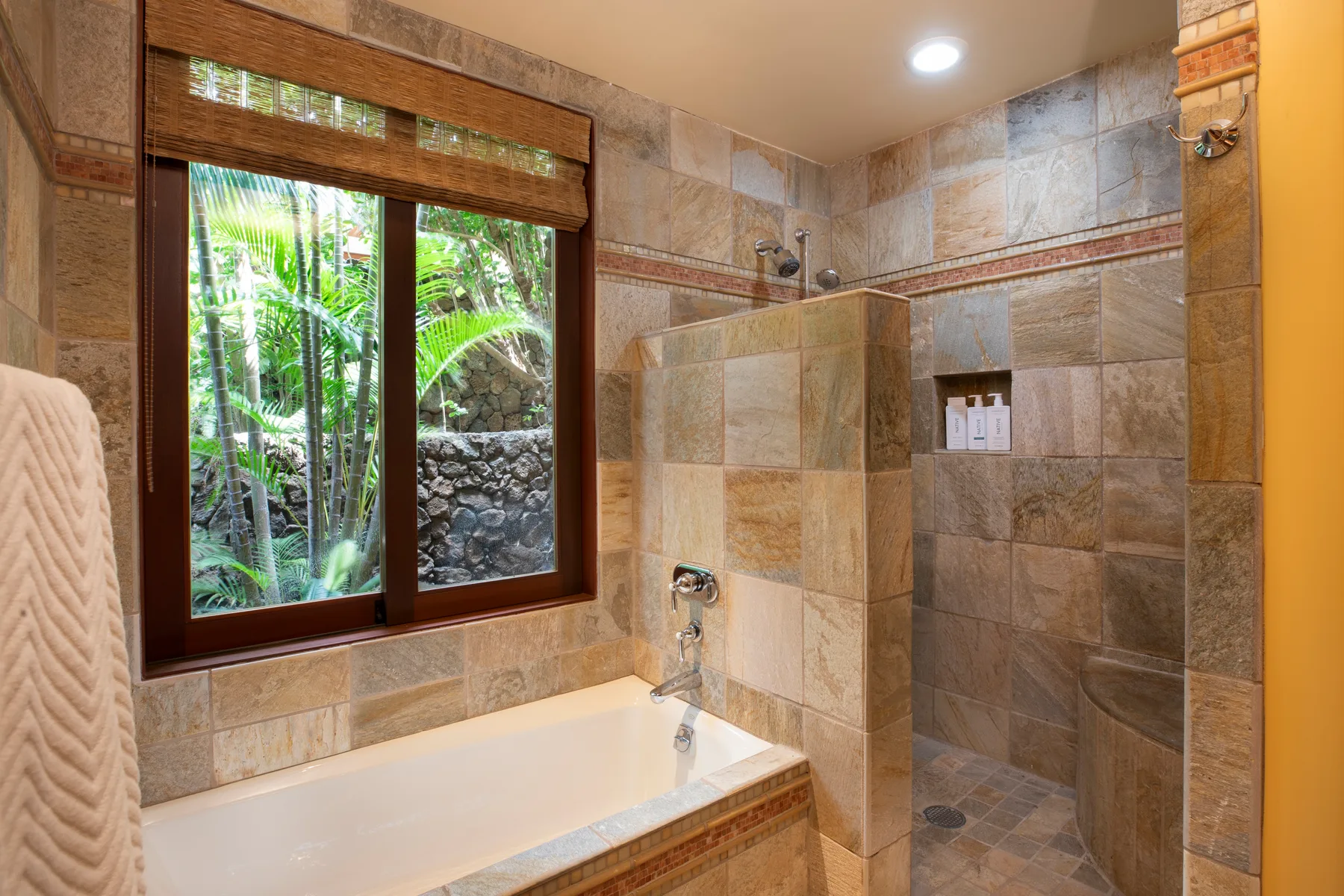 Un baño con azulejos, bañera, ducha y una ventana con vistas a la vegetación.