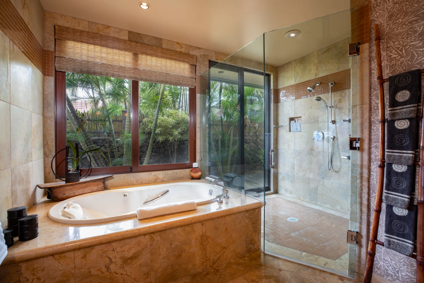 Un baño con azulejos, bañera, ducha de cristal y grandes ventanas con vegetación al otro lado.
