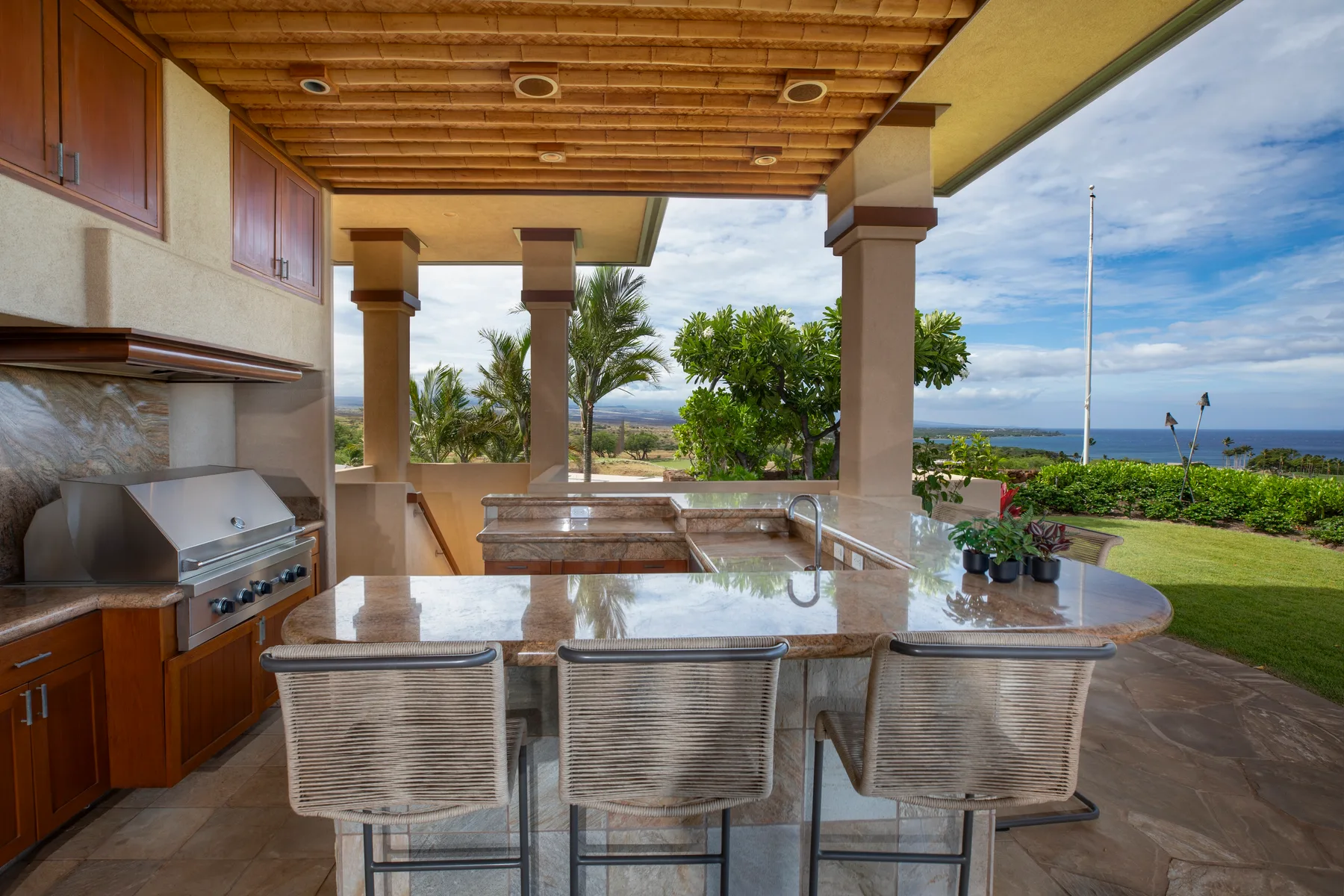 Una cocina y comedor al aire libre se abren a un jardín y una vista costera distante.