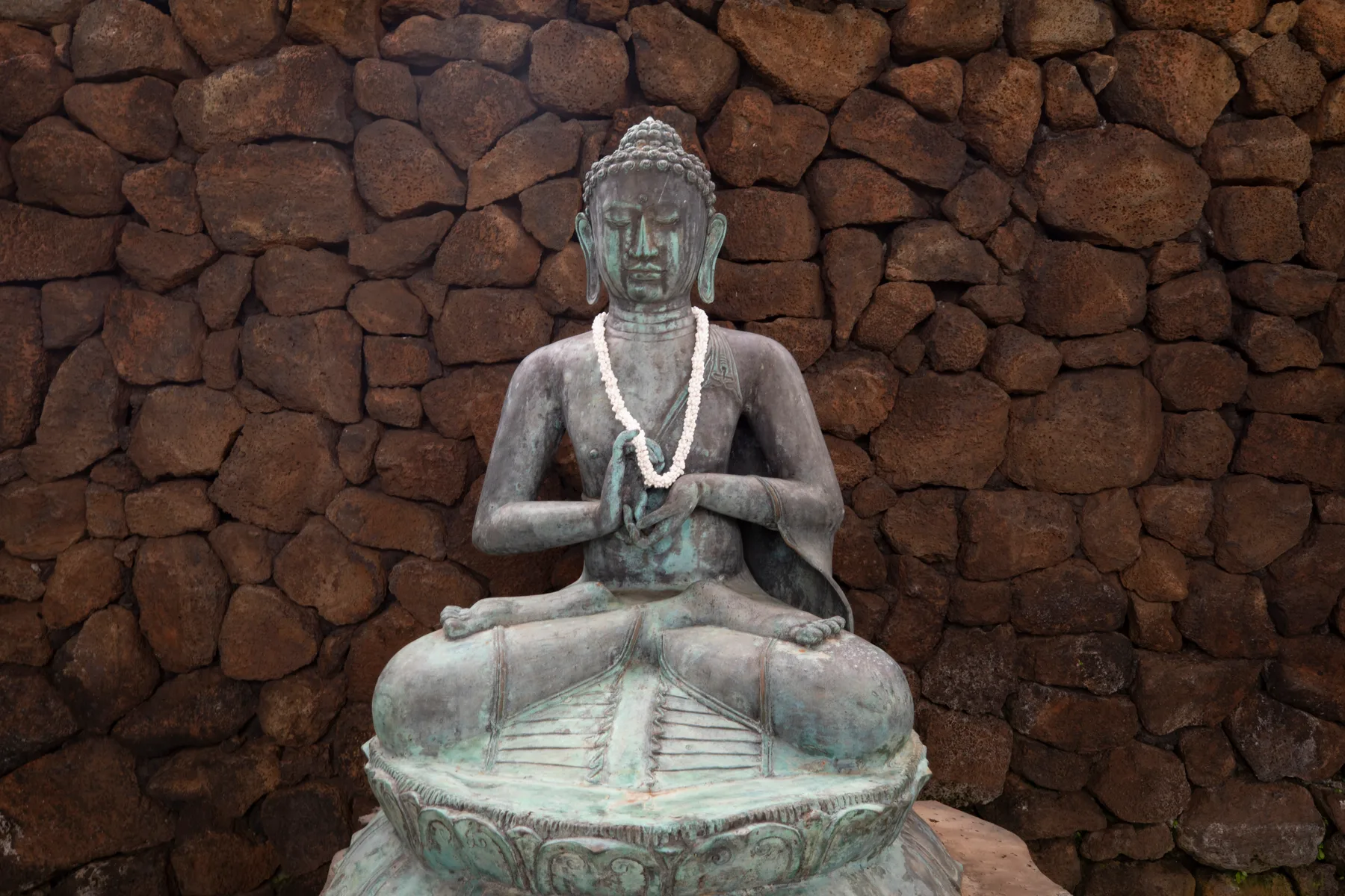 Una estatua sentada con un collar está frente a un muro de piedra irregular.