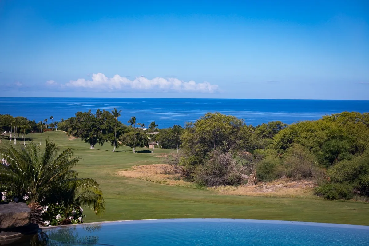 Un paisaje costero con un campo de golf, árboles y el océano al fondo.