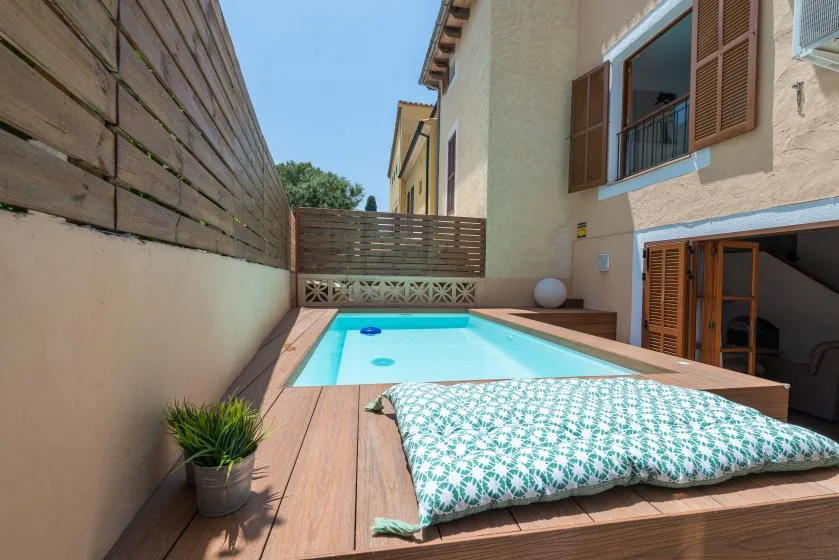 Una pequeña piscina al aire libre junto a una terraza de madera y un edificio claro.