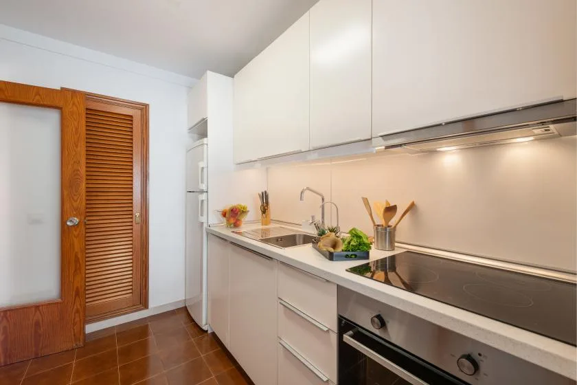 Una cocina luminosa con gabinetes blancos, una encimera larga y una placa de cocina.