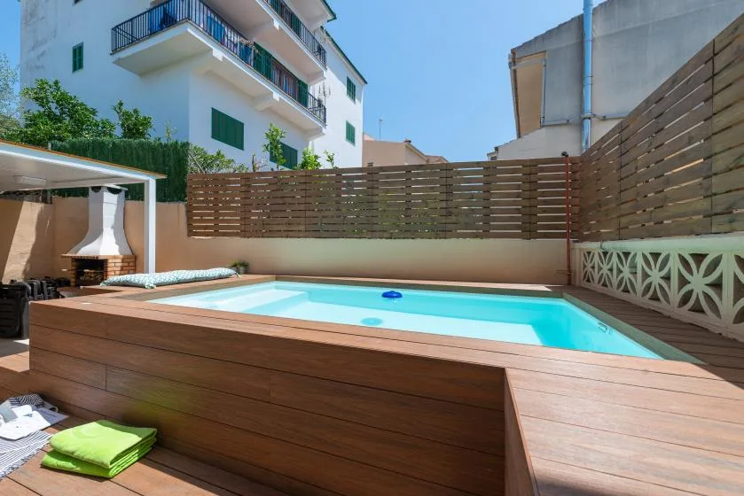 Una pequeña piscina al aire libre está rodeada por una terraza de madera y una valla.