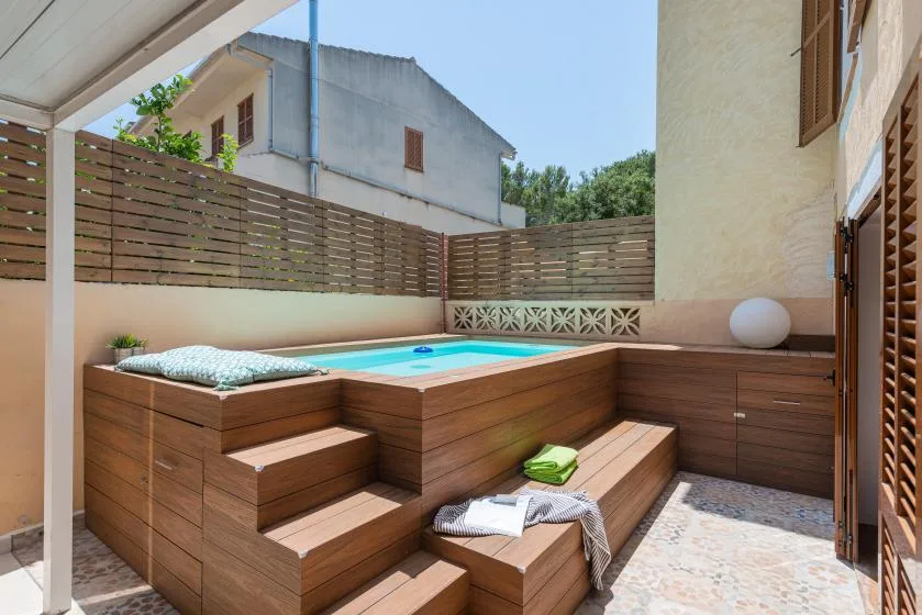 Una pequeña terraza al aire libre tiene una bañera de hidromasaje elevada y asientos de madera integrados.