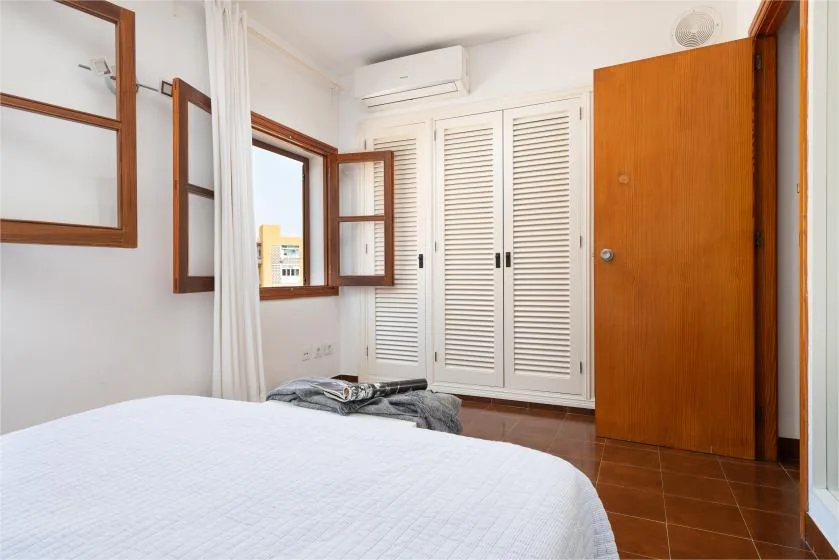 Un dormitorio con una cama, armarios con persianas y una puerta de madera abierta.