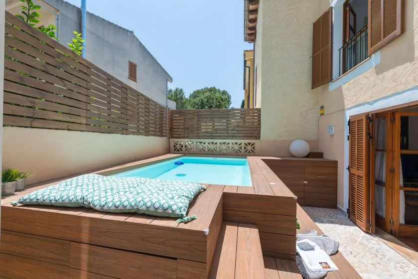 Una pequeña piscina exterior junto a una terraza y un edificio.