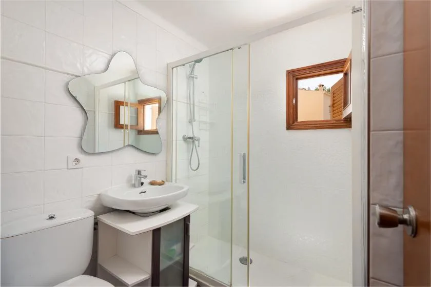 Un baño luminoso con azulejos, lavabo, espejo de pared y ducha de vidrio.