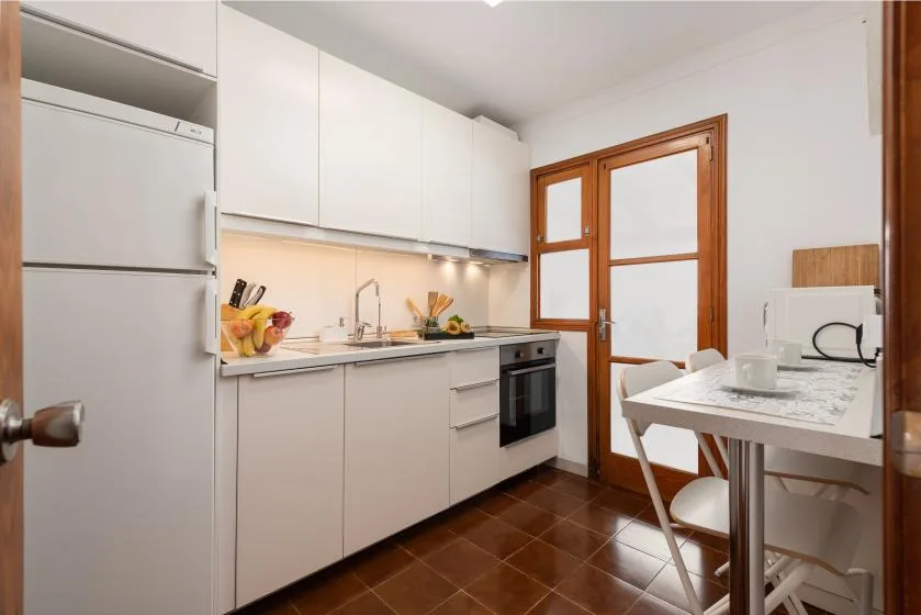 Una cocina compacta con armarios blancos, un refrigerador y una mesa de comedor.