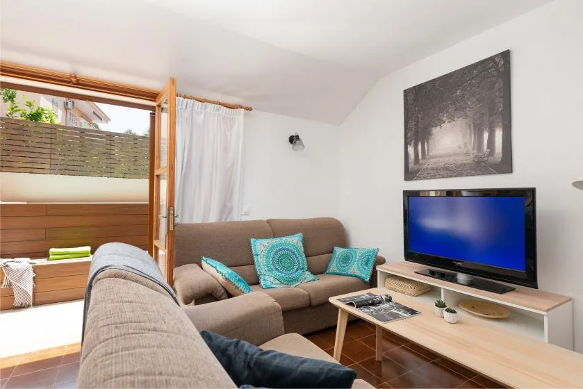 Una sala de estar con asientos, un televisor y una ventana grande.