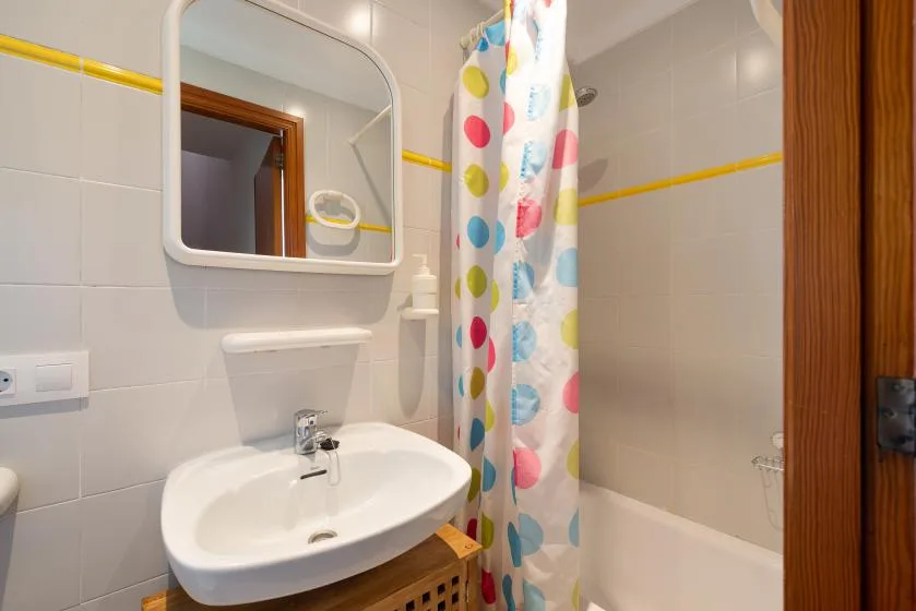 Un baño alicatado con lavabo, espejo y cortina de ducha colorida.