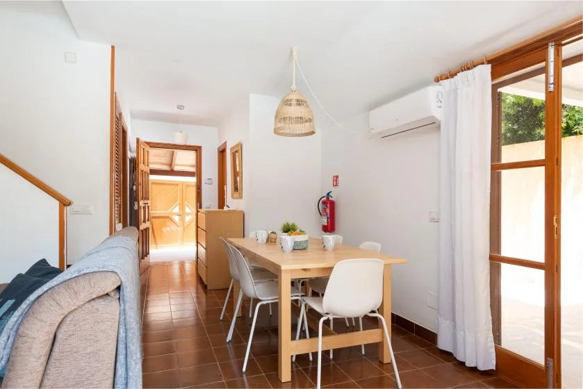 Un comedor con una mesa de madera y sillas junto a puertas de vidrio abiertas.