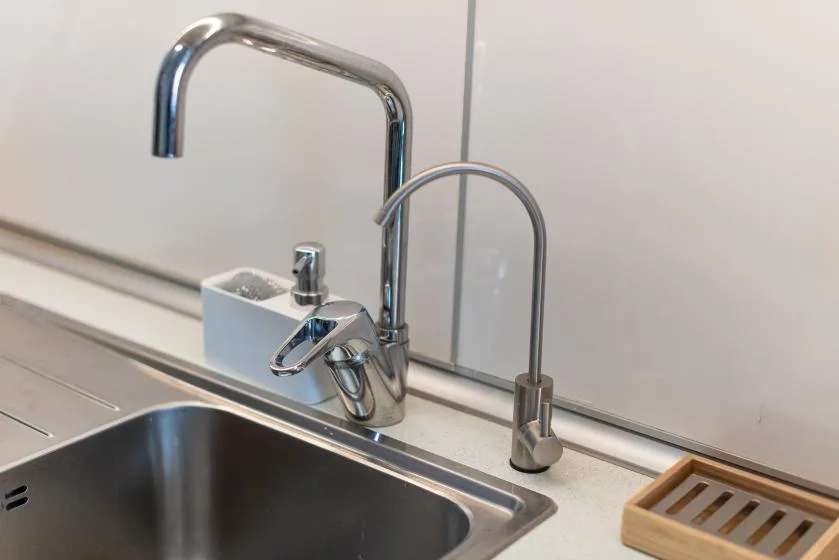 Un fregadero de cocina de acero inoxidable con un grifo alto curvo y un grifo lateral más pequeño.