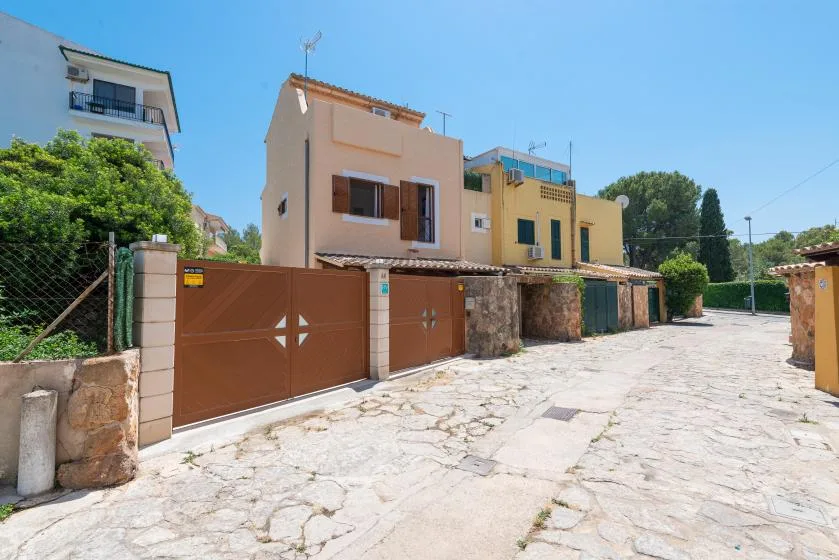 Una calle pavimentada pasa junto a casas en tonos pastel y portones marrones bajo un cielo azul despejado.