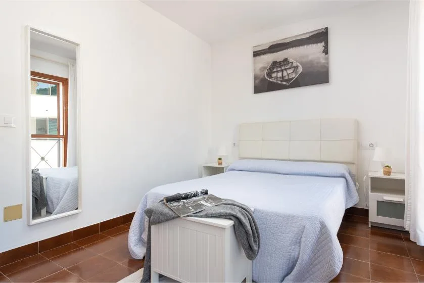 Un dormitorio con una cama bien tendida, mesitas de noche y un cuadro enmarcado.