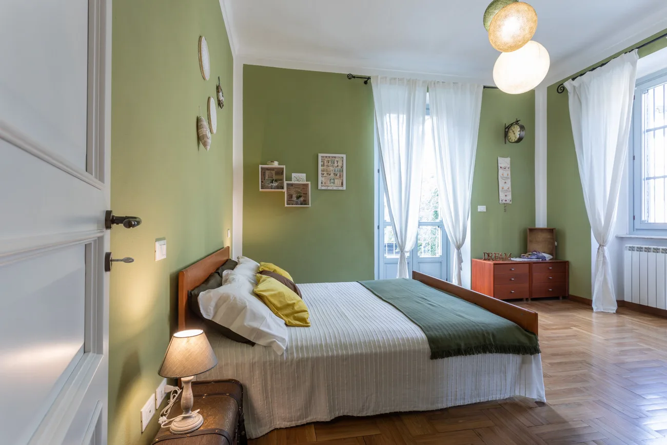 A bedroom with a bed, green walls, and sheer curtains over tall windows.