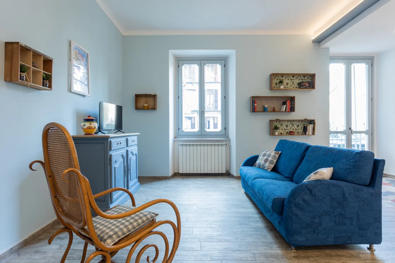A living room with blue seating, a wooden rocking chair, and tall windows.