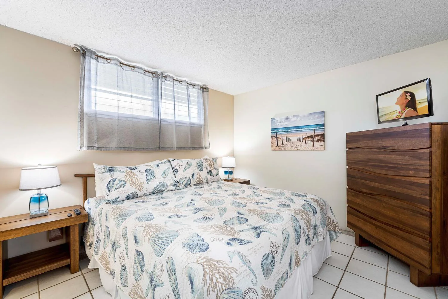 A bedroom with a bed covered in a pale patterned spread and a wooden dresser.