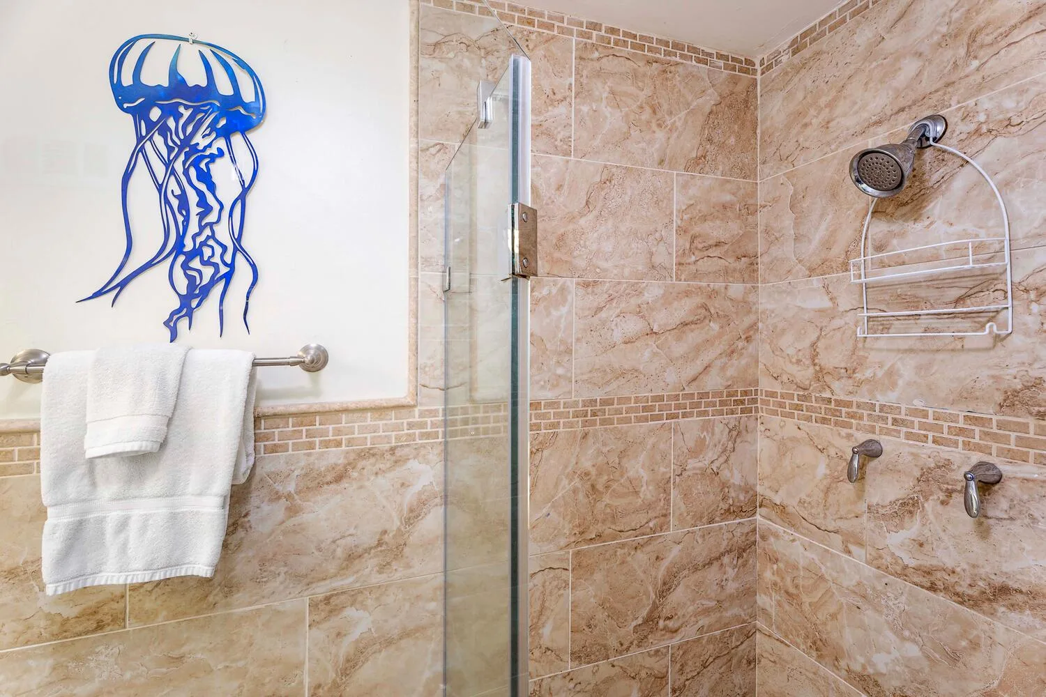 A tiled bathroom shower with a glass divider and wall-mounted showerhead.