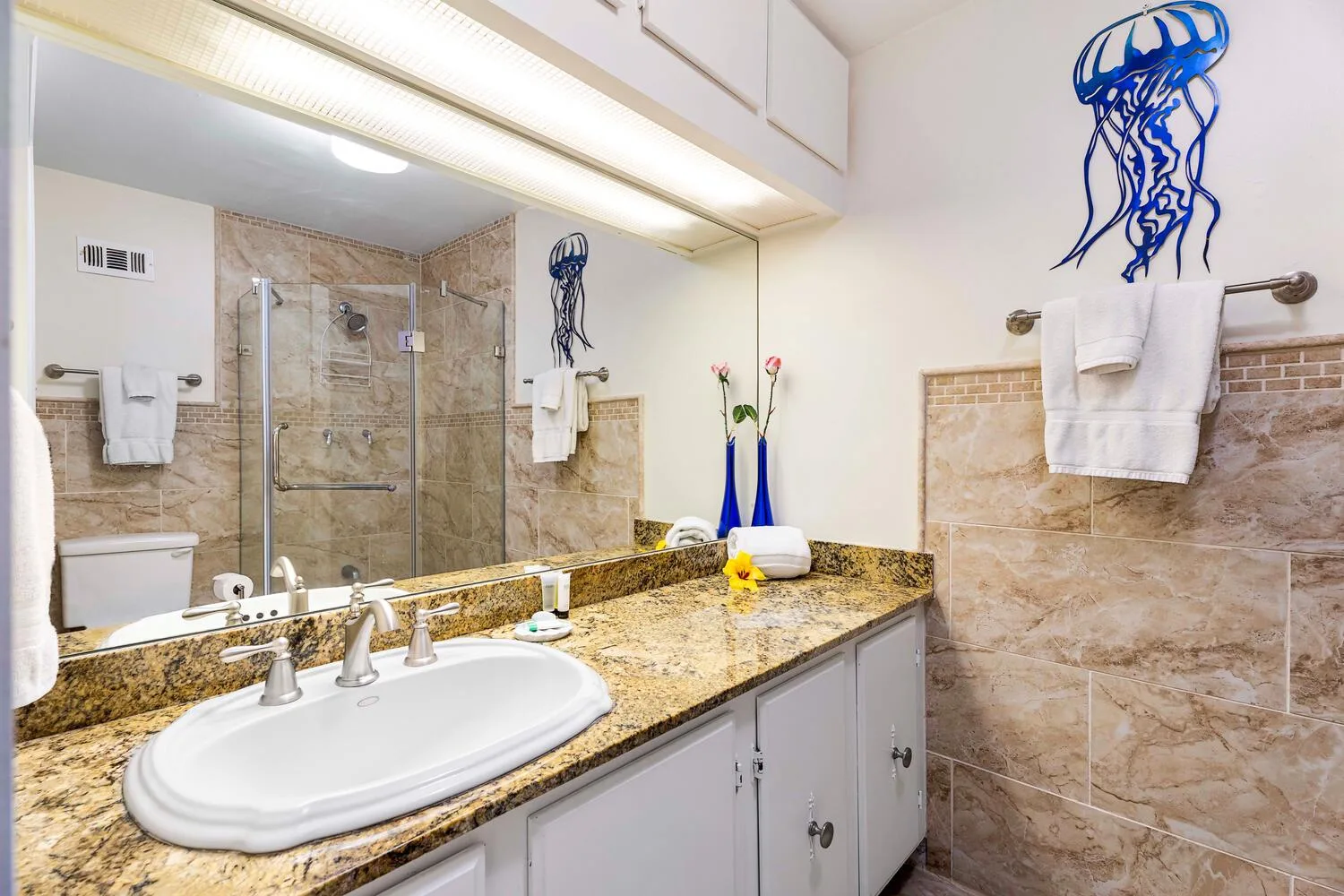 A bathroom vanity with a wide mirror, stone countertop, and tiled walls.