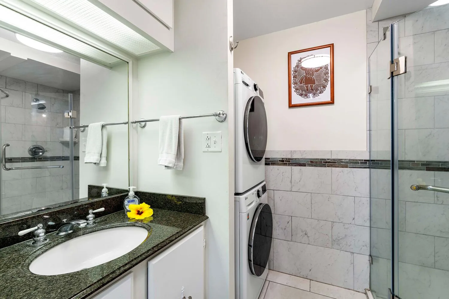 A bathroom with a sink vanity, mirror, and laundry machines.
