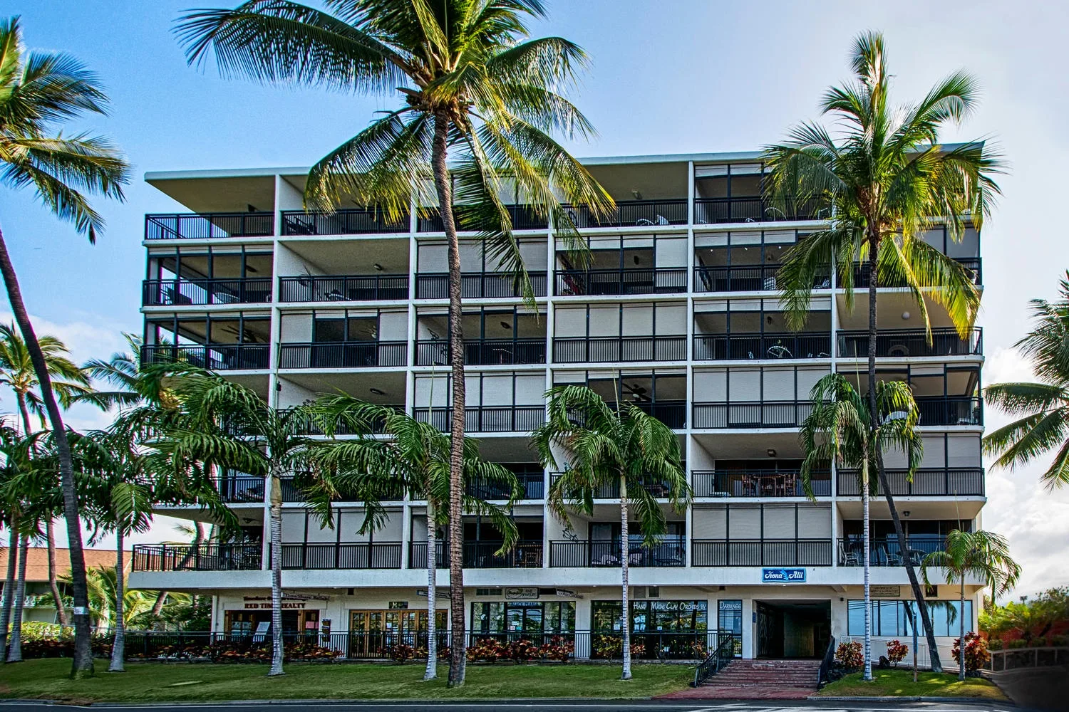 A modern multi-story building stands among palm trees under a clear sky.