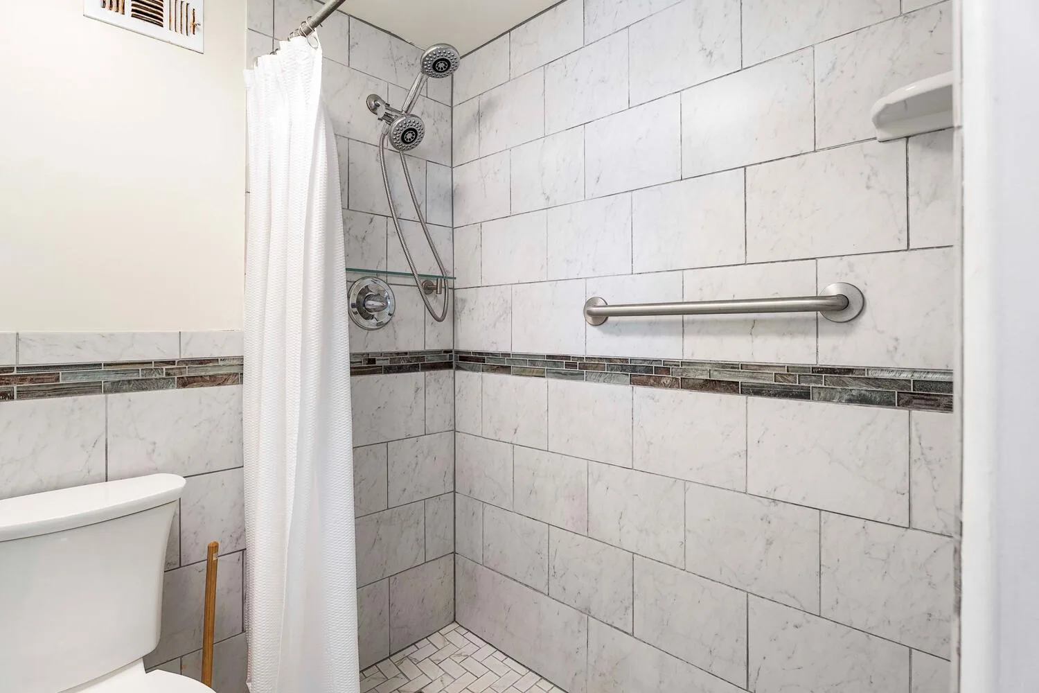 A tiled bathroom shower area with a white curtain and metal grab bar.