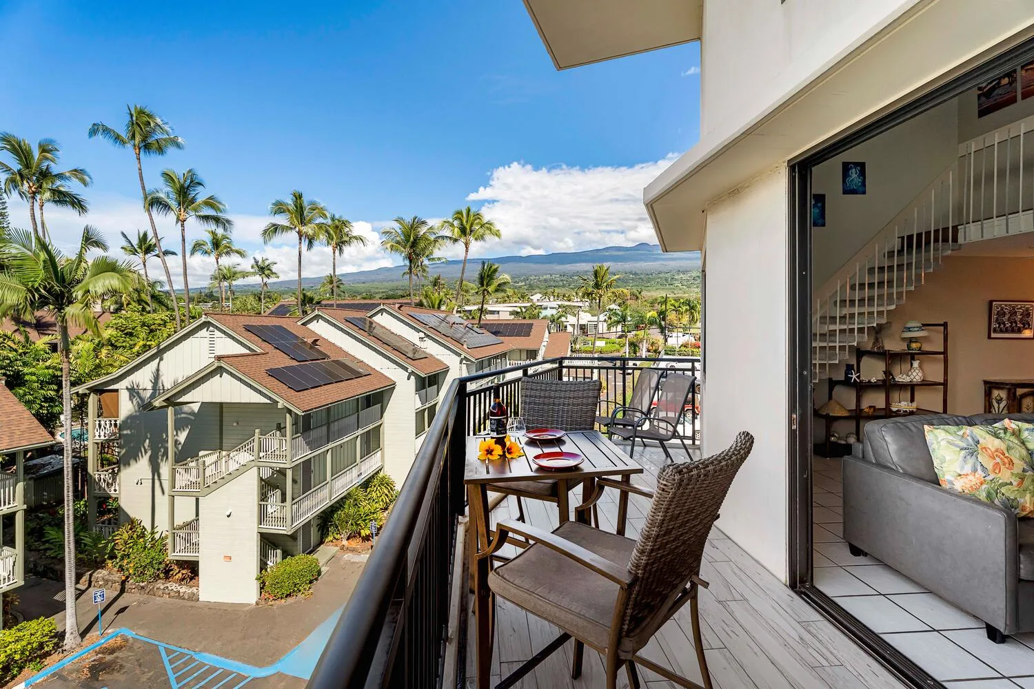 A balcony overlooks nearby homes, palm trees, and distant hills.