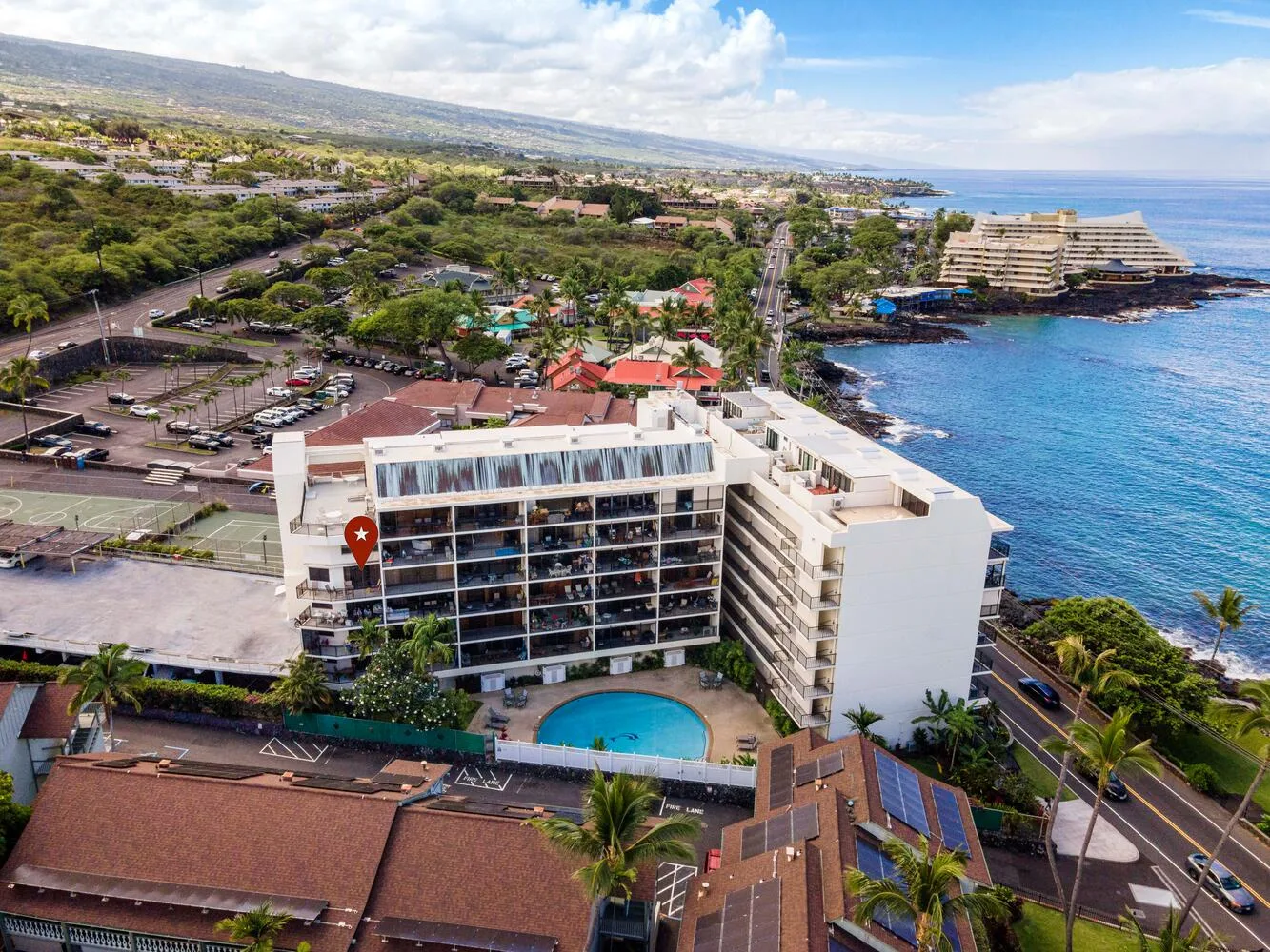 Aerial view of a coastal hotel beside the ocean and a mountain landscape.