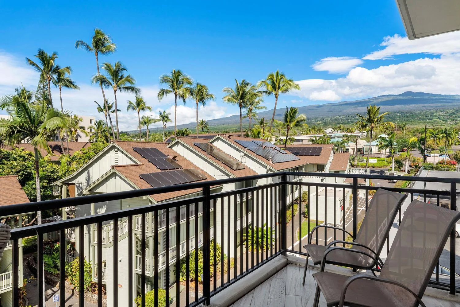 A balcony overlooks nearby homes, palm trees, and distant mountains.