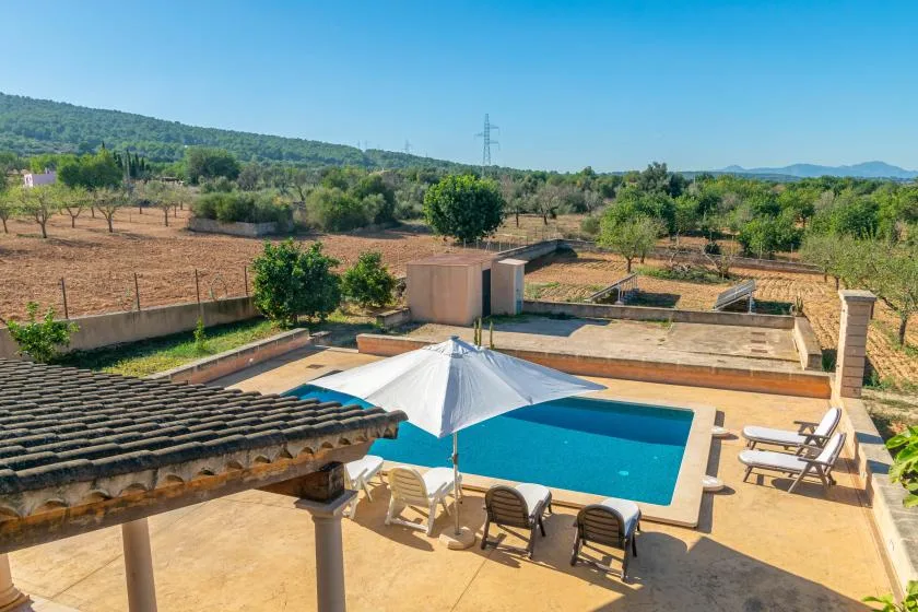 Una piscina al aire libre está junto a un patio con asientos y un paisaje abierto al fondo.