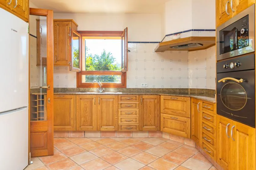 Una cocina con gabinetes de madera, piso de baldosas y una ventana sobre el fregadero.