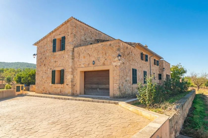 Una casa de piedra se alza junto a una entrada pavimentada bajo un cielo despejado.