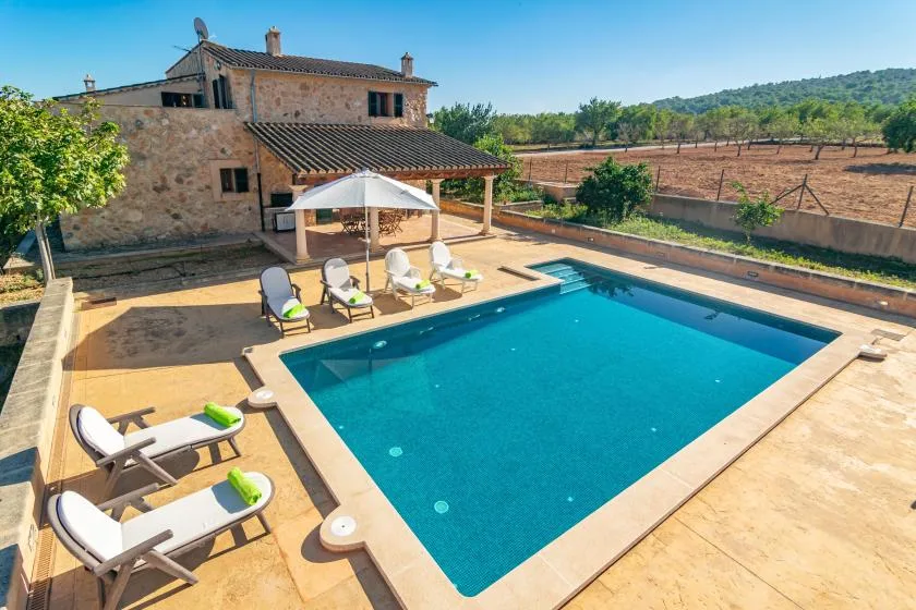 Una piscina al aire libre junto a una casa de piedra, con asientos en la terraza.