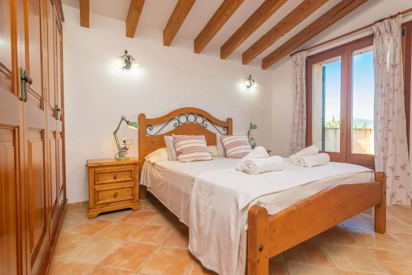 Dormitorio con una cama de madera vestida con ropa blanca junto a una ventana grande.