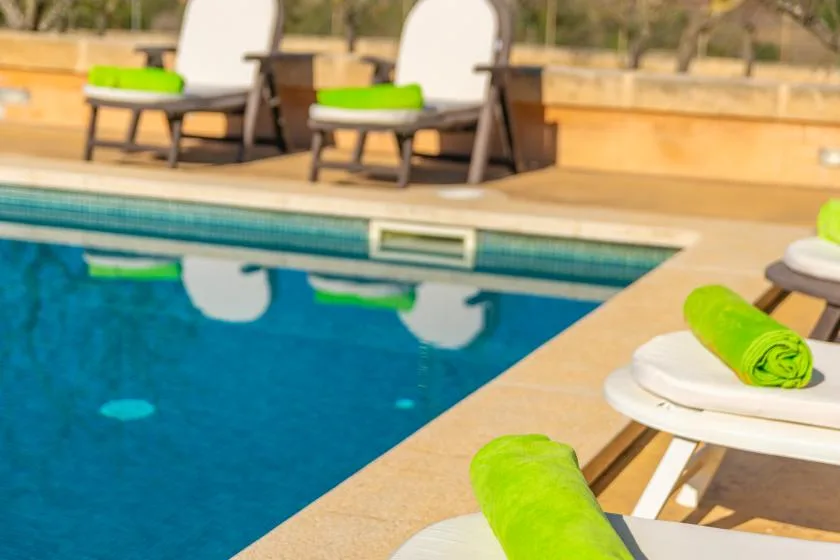 Una piscina con asientos blancos y toallas verde brillante junto al agua.