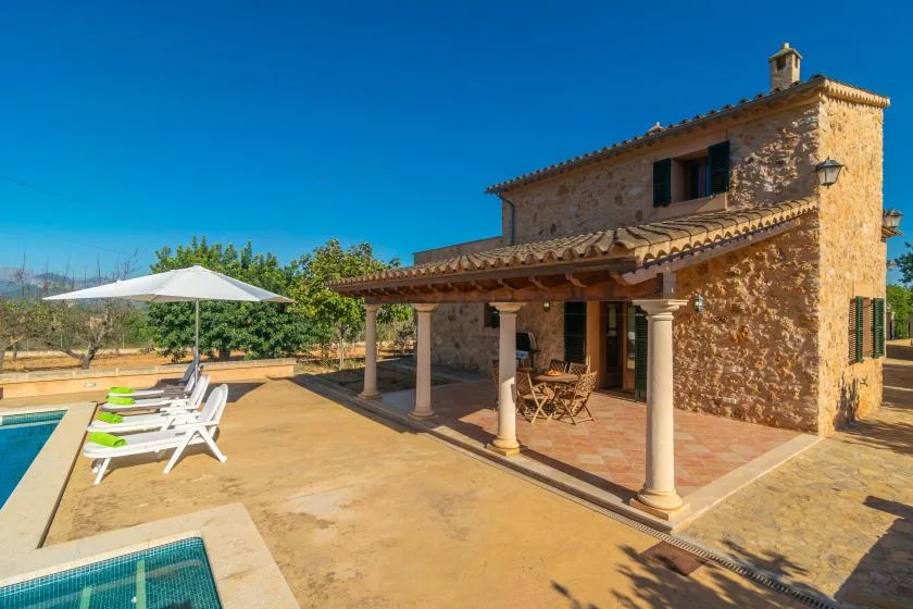 Una casa de piedra con patio cubierto junto a una piscina.