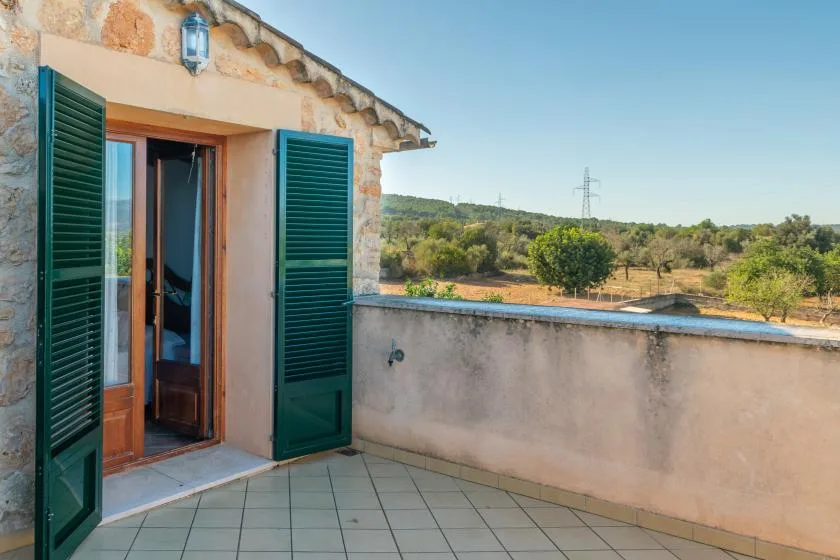 Una terraza de baldosas da a un paisaje rural, con contraventanas verdes abiertas junto a la puerta.