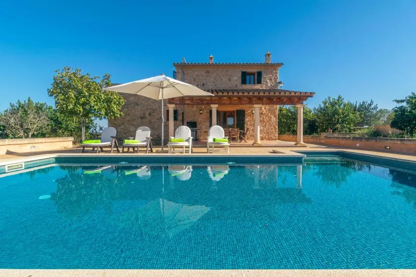 Una piscina frente a una casa de piedra, con asientos en el patio y una sombrilla.