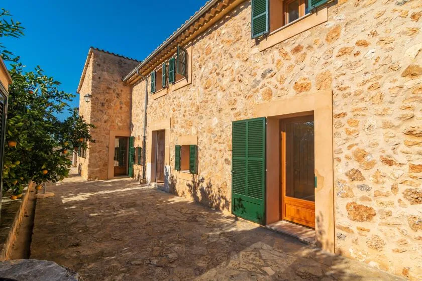 Exterior de un edificio de piedra con contraventanas verdes y patio pavimentado.