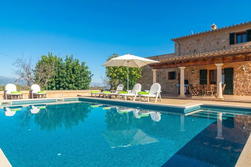 Una piscina al aire libre junto a una casa de piedra, con tumbonas y una sombrilla.