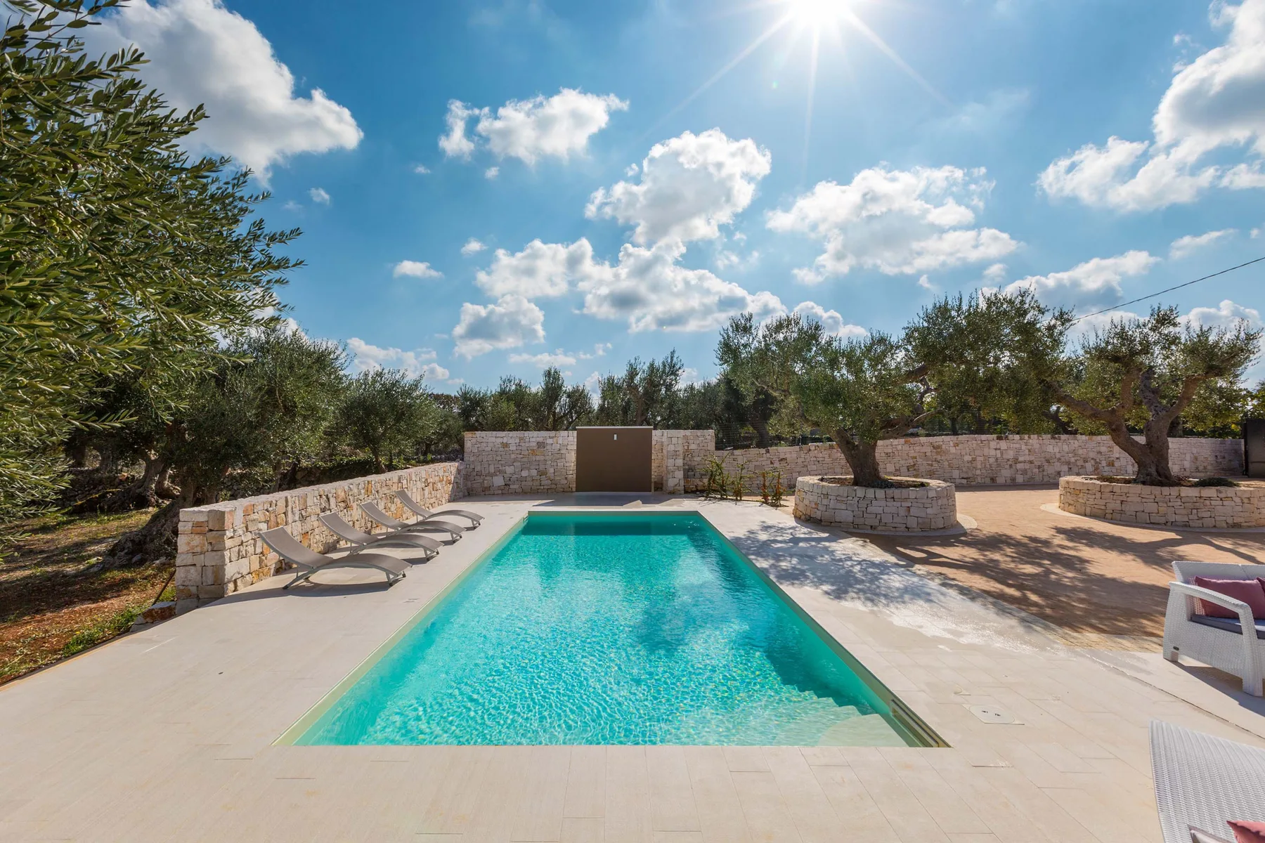 Una piscina al aire libre está en un patio pavimentado rodeado de árboles.
