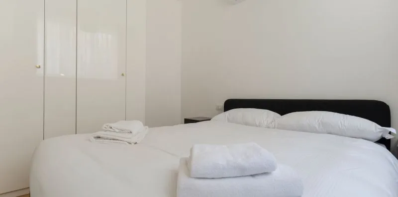 Un dormitorio con ropa de cama blanca, toallas dobladas y un cabecero oscuro.