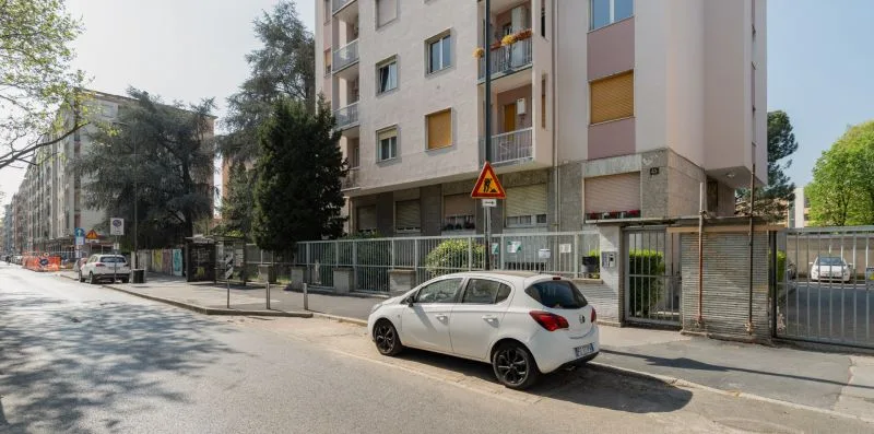 Edificios de apartamentos bordean una calle soleada, con un coche blanco junto a la acera.