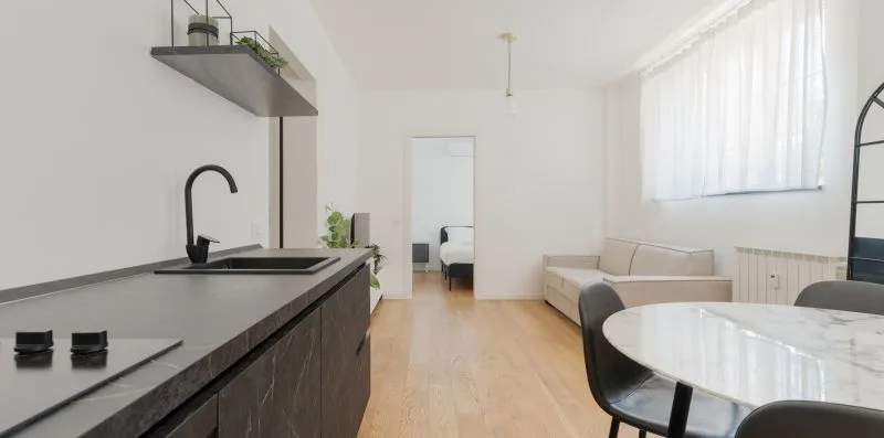Una estancia diáfana y luminosa con una encimera de cocina y una mesa junto a una zona de estar.
