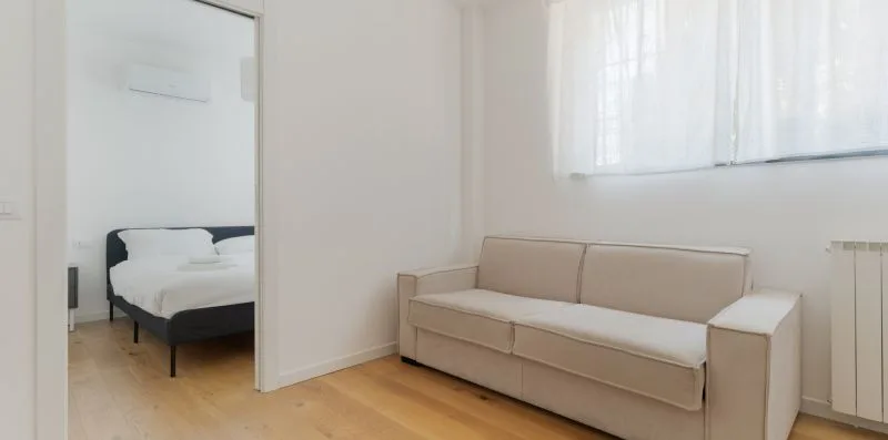 Una sala luminosa con un sofá beige y una ventana con cortinas transparentes.